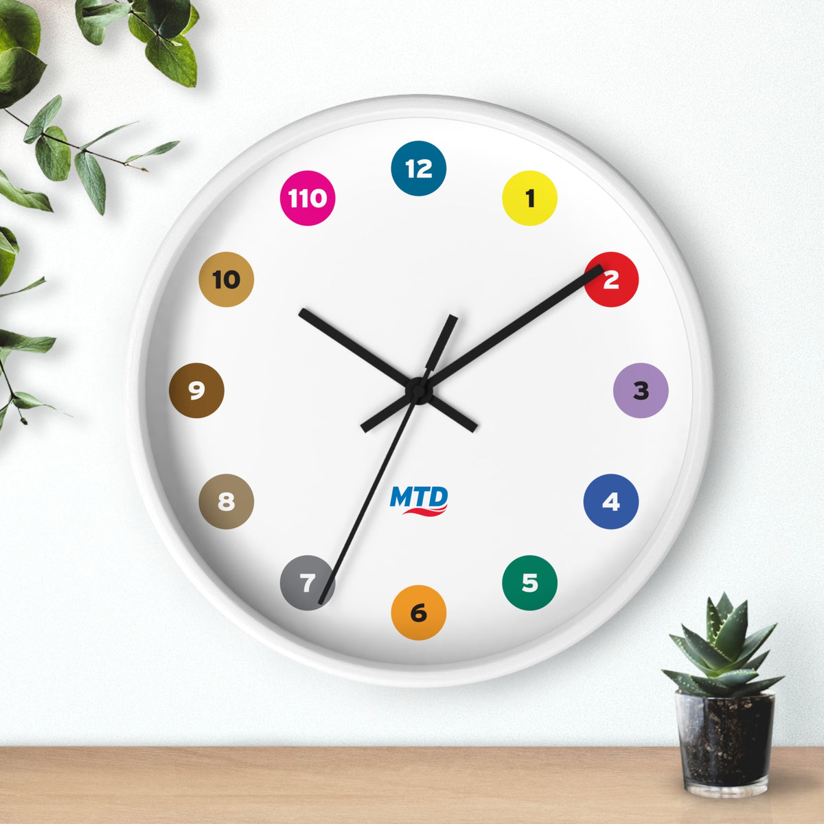 Primary Alt Text Round wall clock featuring colorful MTD route bubbles arranged as hour markers on a white clock face with the MTD logo in the center.