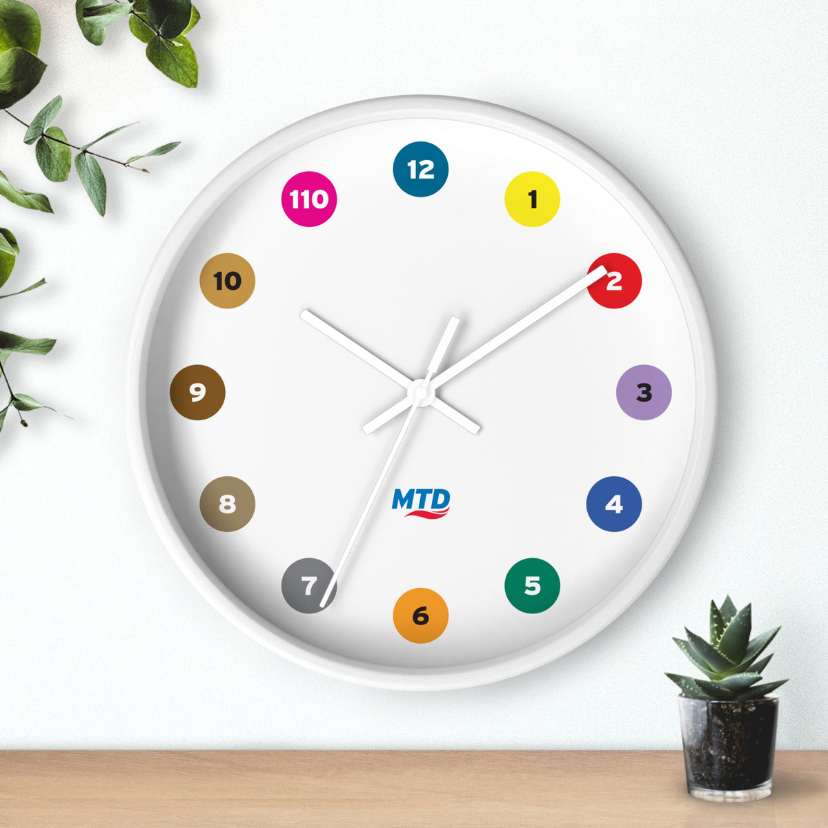 Primary Alt Text Round wall clock featuring colorful MTD route bubbles arranged as hour markers on a white clock face with the MTD logo in the center.