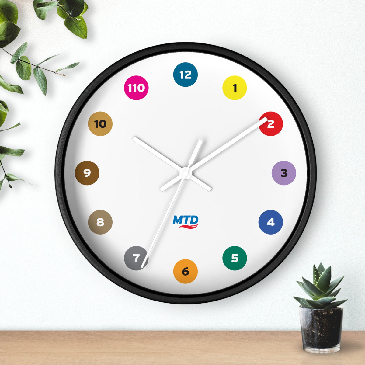 Primary Alt Text Round wall clock featuring colorful MTD route bubbles arranged as hour markers on a white clock face with the MTD logo in the center.
