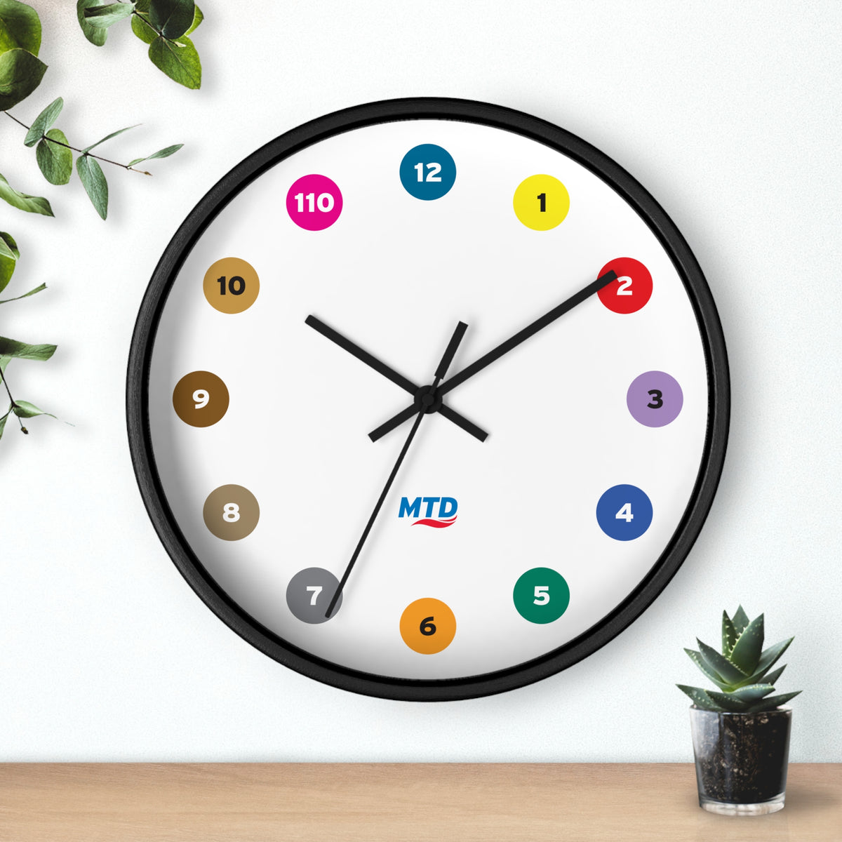 Primary Alt Text Round wall clock featuring colorful MTD route bubbles arranged as hour markers on a white clock face with the MTD logo in the center.