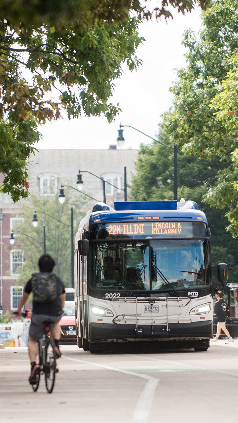A cyclist riding on a tree-lined street with an MTD bus in the background.