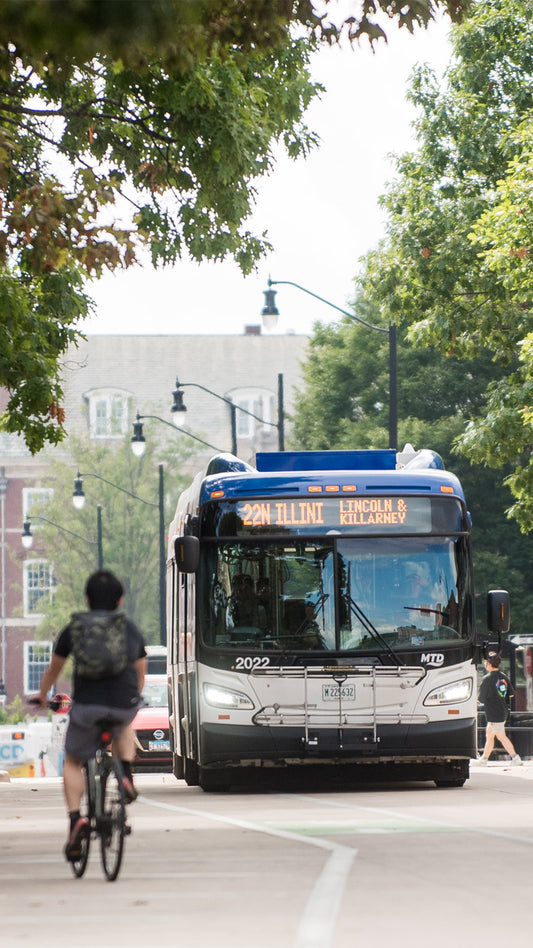 A cyclist riding on a tree-lined street with an MTD bus in the background.